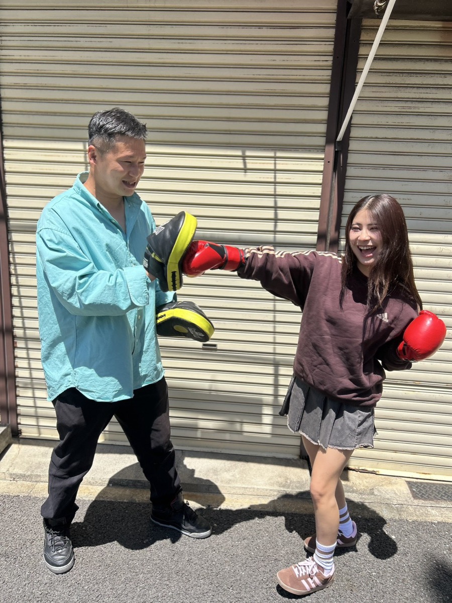 ジムの外で笑顔でミット打ちをする会員とトレーナー