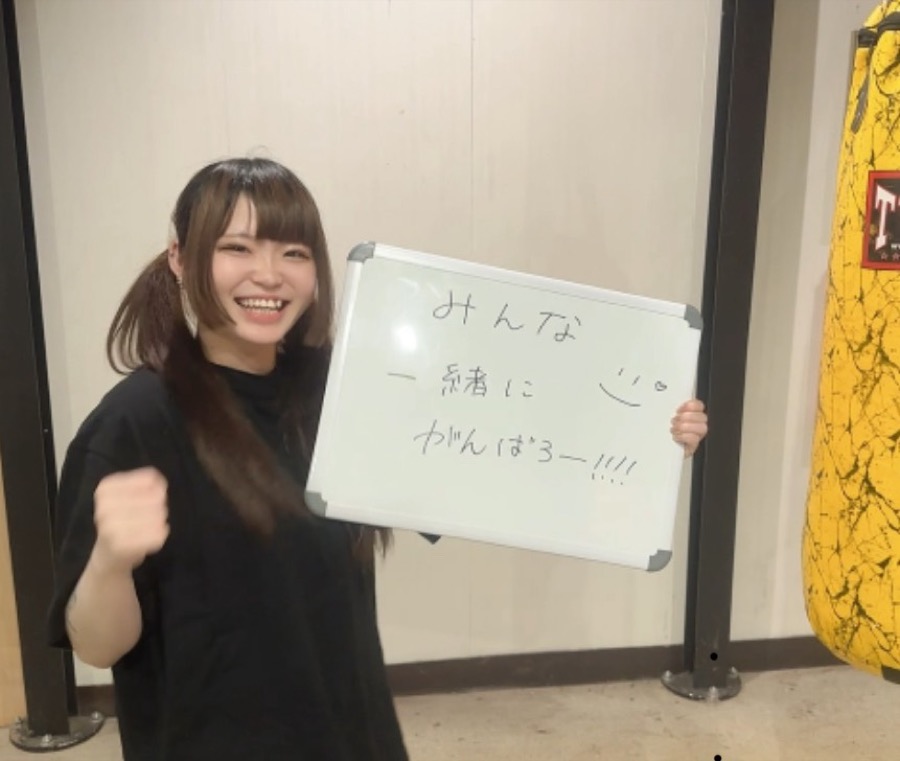 「みんな一緒にがんばろー」と書いたボードを持つ女性会員